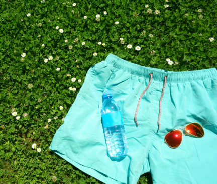 Lyseblå badeshorts på græsplæne med solbriller og vandflaske